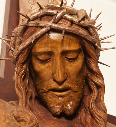 Zdjęcie nr 11: Rzeźbiona figura Chrystusa Ukrzyżowanego zawieszona na prostym, późniejszym od rzeźby krzyżu. Chrustu wisi z rozłożonymi do boków rękami przybitymi gwoździami, ze stopami złożonymi razem, prawa na lewej, przybitymi jednym gwoździem; kolana lekko ugięte. Ciało wyprężone, z zaznaczonymi żebrami i muskulaturą. Głowa opada na prawe ramię, twarz pociągła, oczy przymknięte, proste, nos prosty, długi, usta rozchylone, otoczone krótkimi wąsami i dzieląca się w dwa pukle brodą. Długie, kręcone włosy opadają do przodu, na tors, na głowie masywna, złocona korona cierniowa. Figura bejcowana na kolor ciemnobrązowy. Biodra przewiązane srebrzonym, krótkim perizonium którego zwoje przeplatają się z przodu, a koniec przy prawym udzie zawija się w ekspresyjny zwój. Tkanina układa się w drobne fałdy. Chrystus wisi na drewnianym, ciemnobrązowym krzyżu, w jej górnej części titulus z napisem „I.N./R.I.”.  