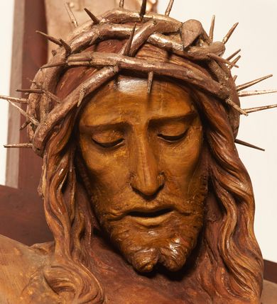 Zdjęcie nr 10: Rzeźbiona figura Chrystusa Ukrzyżowanego zawieszona na prostym, późniejszym od rzeźby krzyżu. Chrustu wisi z rozłożonymi do boków rękami przybitymi gwoździami, ze stopami złożonymi razem, prawa na lewej, przybitymi jednym gwoździem; kolana lekko ugięte. Ciało wyprężone, z zaznaczonymi żebrami i muskulaturą. Głowa opada na prawe ramię, twarz pociągła, oczy przymknięte, proste, nos prosty, długi, usta rozchylone, otoczone krótkimi wąsami i dzieląca się w dwa pukle brodą. Długie, kręcone włosy opadają do przodu, na tors, na głowie masywna, złocona korona cierniowa. Figura bejcowana na kolor ciemnobrązowy. Biodra przewiązane srebrzonym, krótkim perizonium którego zwoje przeplatają się z przodu, a koniec przy prawym udzie zawija się w ekspresyjny zwój. Tkanina układa się w drobne fałdy. Chrystus wisi na drewnianym, ciemnobrązowym krzyżu, w jej górnej części titulus z napisem „I.N./R.I.”.  