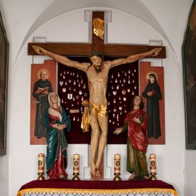 Zdjęcie nr 1: Rzeźba przedstawia Chrystusa Ukrzyżowanego. Postać ukazana jest frontalnie, przybita do krzyża trzema gwoździami z nogami delikatnie ugiętymi w kolanach. Głowa Chrystusa opada na prawe ramię. Sylwetka muskularna z wyraźnie podkreśloną linią żeber i mostka w formie guzów. Twarz podłużna z zamkniętymi oczami, długim i prostym nosem, okolona ciemnobrązową brodą, zwiniętą na końcu w dwa symetryczne pukle. Długie, brązowe włosy opadają na plecy i jednym puklem na prawe ramię. Na głowie Chrystus ma założoną zieloną koronę cierniową. Na prawym boku widać krwawiącą ranę. Podobnie smużki krwi wypływają z ran po gwoździach. Perizonium złocone, przewiązane na prawym boku sznurem i zwisające wzdłuż prawego biodra. W górnej części krzyża znajduje się titulus w formie pionowej banderoli z napisem „IN/RI”. Polichromia w odsłoniętych partiach ciała naturalistyczna. Perizonium i titulus złocone. Krzyż prosty i gładki, malowany na brązowo.

