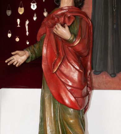 Zdjęcie nr 10: Rzeźba przedstawia Chrystusa Ukrzyżowanego. Postać ukazana jest frontalnie, przybita do krzyża trzema gwoździami z nogami delikatnie ugiętymi w kolanach. Głowa Chrystusa opada na prawe ramię. Sylwetka muskularna z wyraźnie podkreśloną linią żeber i mostka w formie guzów. Twarz podłużna z zamkniętymi oczami, długim i prostym nosem, okolona ciemnobrązową brodą, zwiniętą na końcu w dwa symetryczne pukle. Długie, brązowe włosy opadają na plecy i jednym puklem na prawe ramię. Na głowie Chrystus ma założoną zieloną koronę cierniową. Na prawym boku widać krwawiącą ranę. Podobnie smużki krwi wypływają z ran po gwoździach. Perizonium złocone, przewiązane na prawym boku sznurem i zwisające wzdłuż prawego biodra. W górnej części krzyża znajduje się titulus w formie pionowej banderoli z napisem „IN/RI”. Polichromia w odsłoniętych partiach ciała naturalistyczna. Perizonium i titulus złocone. Krzyż prosty i gładki, malowany na brązowo.

