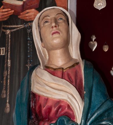 Zdjęcie nr 2: Rzeźba pełnoplastyczna, ustawiona na niskim cokole. Matka Boska stojąca w nieznacznym kontrapoście z dłońmi splecionymi na wysokości pasa oraz głową uniesioną ku górze. Twarz pociągła, nos długi i prosty, małe usta, wzrok skierowany ku górze. Ubrana jest w czerwoną suknię z długimi rękawami, ze złotą lamówką u szyi oraz swobodnie narzucony na ramiona błękitny płaszcz ozdobiony na brzegach analogicznym wykończeniem jak w sukni. Na głowie ma założony biały welon, którego jeden koniec spływa z przodu postaci. Spod szat wystają bose stopy. Polichromia w odsłoniętych partiach ciała naturalistyczna, delikatnie jasna.