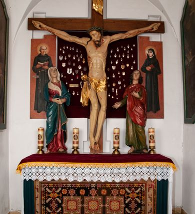 Zdjęcie nr 4: Rzeźba pełnoplastyczna, ustawiona na niskim cokole. Matka Boska stojąca w nieznacznym kontrapoście z dłońmi splecionymi na wysokości pasa oraz głową uniesioną ku górze. Twarz pociągła, nos długi i prosty, małe usta, wzrok skierowany ku górze. Ubrana jest w czerwoną suknię z długimi rękawami, ze złotą lamówką u szyi oraz swobodnie narzucony na ramiona błękitny płaszcz ozdobiony na brzegach analogicznym wykończeniem jak w sukni. Na głowie ma założony biały welon, którego jeden koniec spływa z przodu postaci. Spod szat wystają bose stopy. Polichromia w odsłoniętych partiach ciała naturalistyczna, delikatnie jasna.