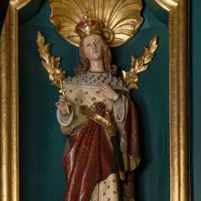 Zdjęcie nr 1: Rzeźba pełnoplastyczna przedstawia św. Kazimierza Królewicza. Święty ukazany jest w pozycji stojącej na niskim cokole, frontalnie, z lewą nogą wysuniętą do przodu. W prawej dłoni trzyma złote berło, lewą ma złożoną na piersi. Twarz podłużna o młodzieńczych rysach, z wyraźnie zaznaczonym podbródkiem, wzrokiem skierowanym przed siebie, okolona długimi i jasnymi włosami, spływającymi równolegle po bokach i symetrycznie podwiniętymi na końcach. Ubrany jest w strój książęcy: długą i białą suknię, obszytą futrem sobolowym, dekorowaną złotymi gwiazdami oraz ciemnoczerwony płaszcz zdobiony wicią akantową z zieloną podszewką, przerzucony swobodnie przez lewe ramię. Na głowie mitra książęca, na stopach buty z wysokimi cholewami, u lewego boku zawieszony na pasie miecz. Polichromia w odsłoniętych partiach ciała naturalistyczna, jasna; berło i detale złocone.

