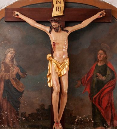 Zdjęcie nr 9: Pełnoplastyczna figura Chrystusa na prostym krzyżu umieszczona na tle malowanego przedstawienia grupy Ukrzyżowania z Marią, św. Janem i z Jerozolimą pośrodku. Rzeźba Chrystusa przybita do krzyża trzema gwoździami, ukazana w typie Cristo morto. Ciało w delikatnym zwisie, sylwetka wydłużona o delikatnie podkreślonej anatomii, nogi lekko ugięte w kolanach. Chrystus ma głowę przechyloną na prawe ramię. Twarz szczupła, z wąskim i długim nosem, zamkniętymi oczami, na wpół otwartymi ustami, okolona krótką brodą, rozdzieloną na końcu w dwa pukle. Włosy długie, spływające na ramiona dwoma skręconymi lokami, na głowie założona korona cierniowa. Perizonium zawiązane na węzeł na prawym boku, z jednym końcem zwisającym wzdłuż prawej nogi, z przodu tworzące fałdy na kształt litery „V”. Z boku, dłoni, stóp i spod korony cierniowej spływają strużki krwi. Polichromia ciała naturalistyczna, perizonium i titulus złocone. Krzyż gładki, nad głową Chrystusa titulus w formie pionowej banderoli z napisem „I.N./R.I.”. 
