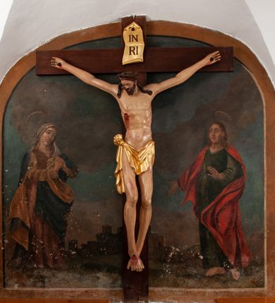 Zdjęcie nr 1: Pełnoplastyczna figura Chrystusa na prostym krzyżu umieszczona na tle malowanego przedstawienia grupy Ukrzyżowania z Marią, św. Janem i z Jerozolimą pośrodku. Rzeźba Chrystusa przybita do krzyża trzema gwoździami, ukazana w typie Cristo morto. Ciało w delikatnym zwisie, sylwetka wydłużona o delikatnie podkreślonej anatomii, nogi lekko ugięte w kolanach. Chrystus ma głowę przechyloną na prawe ramię. Twarz szczupła, z wąskim i długim nosem, zamkniętymi oczami, na wpół otwartymi ustami, okolona krótką brodą, rozdzieloną na końcu w dwa pukle. Włosy długie, spływające na ramiona dwoma skręconymi lokami, na głowie założona korona cierniowa. Perizonium zawiązane na węzeł na prawym boku, z jednym końcem zwisającym wzdłuż prawej nogi, z przodu tworzące fałdy na kształt litery „V”. Z boku, dłoni, stóp i spod korony cierniowej spływają strużki krwi. Polichromia ciała naturalistyczna, perizonium i titulus złocone. Krzyż gładki, nad głową Chrystusa titulus w formie pionowej banderoli z napisem „I.N./R.I.”. 
