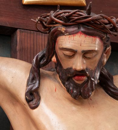 Zdjęcie nr 4: Pełnoplastyczna figura Chrystusa na prostym krzyżu umieszczona na tle malowanego przedstawienia grupy Ukrzyżowania z Marią, św. Janem i z Jerozolimą pośrodku. Rzeźba Chrystusa przybita do krzyża trzema gwoździami, ukazana w typie Cristo morto. Ciało w delikatnym zwisie, sylwetka wydłużona o delikatnie podkreślonej anatomii, nogi lekko ugięte w kolanach. Chrystus ma głowę przechyloną na prawe ramię. Twarz szczupła, z wąskim i długim nosem, zamkniętymi oczami, na wpół otwartymi ustami, okolona krótką brodą, rozdzieloną na końcu w dwa pukle. Włosy długie, spływające na ramiona dwoma skręconymi lokami, na głowie założona korona cierniowa. Perizonium zawiązane na węzeł na prawym boku, z jednym końcem zwisającym wzdłuż prawej nogi, z przodu tworzące fałdy na kształt litery „V”. Z boku, dłoni, stóp i spod korony cierniowej spływają strużki krwi. Polichromia ciała naturalistyczna, perizonium i titulus złocone. Krzyż gładki, nad głową Chrystusa titulus w formie pionowej banderoli z napisem „I.N./R.I.”. 
