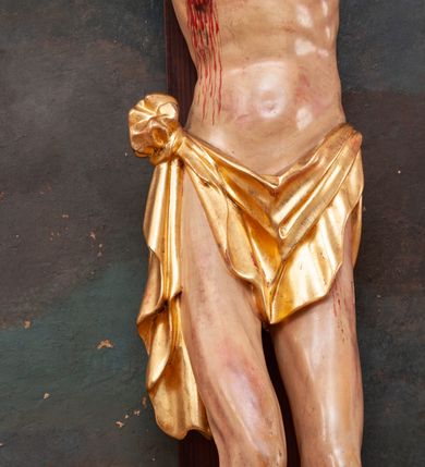 Zdjęcie nr 7: Pełnoplastyczna figura Chrystusa na prostym krzyżu umieszczona na tle malowanego przedstawienia grupy Ukrzyżowania z Marią, św. Janem i z Jerozolimą pośrodku. Rzeźba Chrystusa przybita do krzyża trzema gwoździami, ukazana w typie Cristo morto. Ciało w delikatnym zwisie, sylwetka wydłużona o delikatnie podkreślonej anatomii, nogi lekko ugięte w kolanach. Chrystus ma głowę przechyloną na prawe ramię. Twarz szczupła, z wąskim i długim nosem, zamkniętymi oczami, na wpół otwartymi ustami, okolona krótką brodą, rozdzieloną na końcu w dwa pukle. Włosy długie, spływające na ramiona dwoma skręconymi lokami, na głowie założona korona cierniowa. Perizonium zawiązane na węzeł na prawym boku, z jednym końcem zwisającym wzdłuż prawej nogi, z przodu tworzące fałdy na kształt litery „V”. Z boku, dłoni, stóp i spod korony cierniowej spływają strużki krwi. Polichromia ciała naturalistyczna, perizonium i titulus złocone. Krzyż gładki, nad głową Chrystusa titulus w formie pionowej banderoli z napisem „I.N./R.I.”. 
