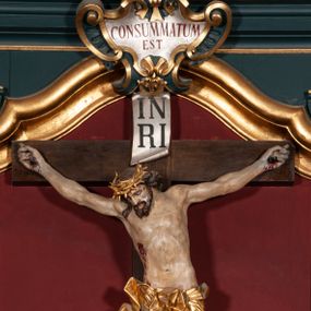 Zdjęcie nr 1: Rzeźba przedstawia Chrystusa Ukrzyżowanego. Postać ukazana jest frontalnie o esowato wygiętej sylwetce, przybita do krzyża trzema gwoździami z nogami ugiętymi w kolanach. Głowa Chrystusa opada na prawe ramię. Sylwetka muskularna z wyraźnie zaznaczoną linią żeber i mostka. Twarz podłużna z niskim czołem, zamkniętymi oczami, długim i prostym nosem oraz wąskimi i lekko rozchylonymi ustami; okolona bujną brodą, zwiniętą na końcu w dwa symetryczne pukle. Długie, brązowe włosy opadają na plecy i prawe ramię, na głowie złota korona cierniowa. Na prawym boku — krwawiąca rana. Podobnie smużki krwi wypływają z ran po gwoździach. Perizonium złocone, silnie drapowane o mocno łamanych fałdach. W górnej części krzyża titulus w formie pionowej banderoli z napisem „IN/RI”. Polichromia w odsłoniętych partiach ciała naturalistyczna. Korona i perizonium złocone, titulus srebrzony. Krzyż prosty i gładki, malowany na brązowo.
