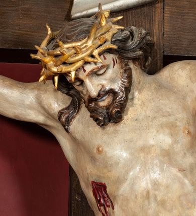 Zdjęcie nr 7: Rzeźba przedstawia Chrystusa Ukrzyżowanego. Postać ukazana jest frontalnie o esowato wygiętej sylwetce, przybita do krzyża trzema gwoździami z nogami ugiętymi w kolanach. Głowa Chrystusa opada na prawe ramię. Sylwetka muskularna z wyraźnie zaznaczoną linią żeber i mostka. Twarz podłużna z niskim czołem, zamkniętymi oczami, długim i prostym nosem oraz wąskimi i lekko rozchylonymi ustami; okolona bujną brodą, zwiniętą na końcu w dwa symetryczne pukle. Długie, brązowe włosy opadają na plecy i prawe ramię, na głowie złota korona cierniowa. Na prawym boku — krwawiąca rana. Podobnie smużki krwi wypływają z ran po gwoździach. Perizonium złocone, silnie drapowane o mocno łamanych fałdach. W górnej części krzyża titulus w formie pionowej banderoli z napisem „IN/RI”. Polichromia w odsłoniętych partiach ciała naturalistyczna. Korona i perizonium złocone, titulus srebrzony. Krzyż prosty i gładki, malowany na brązowo.
