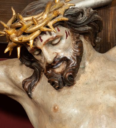 Zdjęcie nr 4: Rzeźba przedstawia Chrystusa Ukrzyżowanego. Postać ukazana jest frontalnie o esowato wygiętej sylwetce, przybita do krzyża trzema gwoździami z nogami ugiętymi w kolanach. Głowa Chrystusa opada na prawe ramię. Sylwetka muskularna z wyraźnie zaznaczoną linią żeber i mostka. Twarz podłużna z niskim czołem, zamkniętymi oczami, długim i prostym nosem oraz wąskimi i lekko rozchylonymi ustami; okolona bujną brodą, zwiniętą na końcu w dwa symetryczne pukle. Długie, brązowe włosy opadają na plecy i prawe ramię, na głowie złota korona cierniowa. Na prawym boku — krwawiąca rana. Podobnie smużki krwi wypływają z ran po gwoździach. Perizonium złocone, silnie drapowane o mocno łamanych fałdach. W górnej części krzyża titulus w formie pionowej banderoli z napisem „IN/RI”. Polichromia w odsłoniętych partiach ciała naturalistyczna. Korona i perizonium złocone, titulus srebrzony. Krzyż prosty i gładki, malowany na brązowo.
