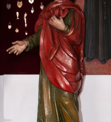 Zdjęcie nr 1: Pełnoplastyczna, polichromowana figura św. Jana ustawiona na niewielkim cokole. Święty ukazany w delikatnym kontrapoście z lewą nogą ugiętą w kolanie, głową uniesioną do góry. Prawą rękę ma wyciągniętą w bok, lewą złożoną na piersi podtrzymuje udrapowaną połę płaszcza. Święty o młodzieńczej fizjonomii, z długimi rozwianymi włosami skręcającymi się w bujne loki po bokach. Twarz pozbawiona zarostu, oczy skierowane ku górze, półkoliste łuki brwiowe. Ubrany jest  w długą, zieloną suknię opadającą prostymi fałdami oraz czerwony płaszcz zarzucony na ramiona, udrapowany na piersi, zawinięty pod lewą ręką. Spod szat wystają bose stopy. Polichromia w odsłoniętych partiach ciała naturalistyczna.