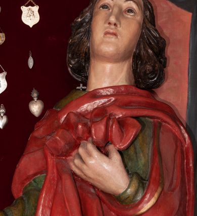 Zdjęcie nr 2: Pełnoplastyczna, polichromowana figura św. Jana ustawiona na niewielkim cokole. Święty ukazany w delikatnym kontrapoście z lewą nogą ugiętą w kolanie, głową uniesioną do góry. Prawą rękę ma wyciągniętą w bok, lewą złożoną na piersi podtrzymuje udrapowaną połę płaszcza. Święty o młodzieńczej fizjonomii, z długimi rozwianymi włosami skręcającymi się w bujne loki po bokach. Twarz pozbawiona zarostu, oczy skierowane ku górze, półkoliste łuki brwiowe. Ubrany jest  w długą, zieloną suknię opadającą prostymi fałdami oraz czerwony płaszcz zarzucony na ramiona, udrapowany na piersi, zawinięty pod lewą ręką. Spod szat wystają bose stopy. Polichromia w odsłoniętych partiach ciała naturalistyczna.
