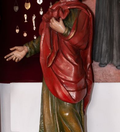 Zdjęcie nr 4: Pełnoplastyczna, polichromowana figura św. Jana ustawiona na niewielkim cokole. Święty ukazany w delikatnym kontrapoście z lewą nogą ugiętą w kolanie, głową uniesioną do góry. Prawą rękę ma wyciągniętą w bok, lewą złożoną na piersi podtrzymuje udrapowaną połę płaszcza. Święty o młodzieńczej fizjonomii, z długimi rozwianymi włosami skręcającymi się w bujne loki po bokach. Twarz pozbawiona zarostu, oczy skierowane ku górze, półkoliste łuki brwiowe. Ubrany jest  w długą, zieloną suknię opadającą prostymi fałdami oraz czerwony płaszcz zarzucony na ramiona, udrapowany na piersi, zawinięty pod lewą ręką. Spod szat wystają bose stopy. Polichromia w odsłoniętych partiach ciała naturalistyczna.