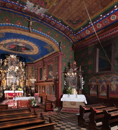 Zdjęcie nr 6: Polichromia o charakterze figuralnym i geometryczno-roślinnym pokrywa ściany i sklepienia prezbiterium, nawy, zakrystii i kruchty zachodniej. Wszystkie ściany prezbiterium do wysokości gzymsu dekorowane są pionowymi, układającymi się naprzemiennie pasami ornamentu roślinno-geometrycznego. Jeden z nich jest granatowy o motywie złotych liści dębu układających się w rozetę z ornamentem geometrycznym. Drugi pas jest żółty z motywem stylizowanych fioletowych i różowych kwiatów o zgeometryzowanych detalach. Gzyms prezbiterium i nawy w kolorze czerwonym, na nim złoty geometryczny pas oraz ornament z granatowych falistych linii wypełnionych w środku białymi punktami. 
Sklepienie prezbiterium jest niebieskie, obramione żółtym pasem z zieloną wicią roślinną, na której ułożone są naprzemiennie granatowe i różowe kwiaty. W narożach stylizowane bukiety kwiatów w kolorach zieleni, brązu i żółci. W centrum sklepienia okrągły medalion ze św. Kingą i Bolesławem Wstydliwym na tle pejzażu wielickiego z kościołem i zamkiem żupnym w oddali. Na pierwszym planie św. Kinga zwrócona jest w swoją prawą stronę, z uniesioną głową. W lewej ręce trzyma pastorał, w prawej wyciągniętej pierścień. Święta ubrana jest w czarny habit klaryski ze szkaplerzem, białą podwiką i welonem oraz czarnym płaszczem z czerwoną podszewką. Na piersi ma złoty łańcuch, na głowie mitrę książęcą. Po prawej stronie św. Kingi klęczy Bolesław Wstydliwy, który obiema rękami trzyma przy rękojeści wbity w ziemię miecz, opleciony skórzanym pasem. Książę ubrany jest w zbroję, niebieską tunikę i czerwony płaszcz spięty złotą fibulą. Na głowie ma kaptur kolczy i hełm z otwartą koroną. Medalion ze sceną ujęty jest żółtą ramą wypełnioną stylizowaną wicią roślinną z naprzemiennie występującymi granatowymi i różowymi kwiatami. Krawędź zewnętrza ozdobiona srebrzystym wieńcem z naprzemiennie ułożonego trójliścia i płomyka. 
Wszystkie ściany nawy pokryte są stylizowanym ornamentem roślinnym składającym się z zielonej wici roślinnej układającej się w regularne medaliony, w których znajdują się kwiaty czerwonego maku. 
Na ścianie północnej w dolnym pasie, pod oknem sześć ostrołukowych arkad na stylizowanych kolumienkach. W pierwszej arkadzie od strony prezbiterium postać klęczącej zakonnicy z opuszczonymi, splecionymi dłońmi, która ubrana jest w biały habit norbertański ze szkaplerzem i brązowy płaszcz z kapturem. U dołu w żółtym polu napis „S(wię)ta BRONISŁAWA”. W drugiej arkadzie królewicz klęczący przy pulpicie, zwrócony w stronę prezbiterium, w obszernym czerwonym płaszczu podbitym futrem i mitrze na głowie. U dołu w żółtym polu napis „S(wię)ty KAZIMIERZ Królewic(z)” W trzeciej arkadzie zwrócona frontalnie siedząca postać z pochyloną głową, ubrana w biały habit zakonny z czarnym płaszczem. U dołu w żółtym polu napis „Bł(ogosławiona) SALOMEA”. W następnych dwóch arkadach występuje stylizowany ornament roślinny z czterema rozetami i ze srebrnym orłem z dwiema tarczami herbowymi, pierwsza z krzyżem na piersi, druga z herbem Szreniawa poniżej. Pole szóstej arkady bez dekoracji. 
Na ścianie południowej w dolnym pasie, pod oknem trzy analogiczne arkady. W pierwszej arkadzie od strony prezbiterium frontalnie siedząca postać w stroju biskupa: białej albie, ciemnoróżowej komży z żółtą lamówką, żółtej kapie i paliuszu, na głowie ma infułę. U dołu w żółtym polu napis „Bł(ogosławiony) WINC(ENTY) KADŁUBEK”. W drugiej arkadzie  postać ukazana w pozycji stojącej, zwróconej w stronę prezbiterium, w prawej ręce trzyma pastorał, lewa w geście błogosławieństwa, ubrana w analogiczny jak poprzednia strój biskupi. U dołu w żółtym polu napis „S(wię)ty STANISŁAW SZCZEP(ANOWSKI)”. W trzeciej arkadzie frontalnie siedząca postać w stroju biskupa: ciemnoróżowej albie, żółtym ornacie, paliuszu, na głowie ma infułę. W  prawej ręce trzyma pastorał, w lewej miniaturę kościoła Mariackiego w Krakowie. Pod nim napis „Bł(ogosławiony) IVO ODROWĄŻ”. 
Sklepienie nawy ujęte ramą złożoną z kilku pasów. Zewnętrzny podzielony na kwadratowe pola, w których naprzemiennie występują dekoracyjny krzyż z kaboszonami i splecionymi literami „MS” oraz wpisany w koło czworoliść z trzema kilofami. Wewnętrzny pas jest zielony dekorowany srebrzonymi kołami, wydzielony zieloną i żółtą falowaną wstęgą. Pośrodku wschodniego pasa obramienia, przy łuku tęczowym znajduje się srebrzony orzeł z tarczą herbową z krzyżem na piersi i tarczą z herbem Szreniawa u dołu. W szponach trzyma trzy kilofy oraz wagę. U dołu znajduje się wstęga z napisem „Arma regiae liberae montanaequae / civitatis Vielicensis”. 
W centrum sklepienia nawy medalion ujęty zewnętrzną ramą utworzoną z grotów i płomieni oraz wewnętrzną z przeplatających się spiralnie wici roślinnych. W polu przedstawienie męczeństwa św. Sebastiana. Postać zwrócona w trzech czwartych w lewo, o bezwładnie opadającym ciele przywiązanym za ramiona i ugięte nogi do drzewa. Wokół głowy nimb zamknięty. Święty przesłonięty w partii podbrzusza białą draperią opadającą na ziemię, po bokach postaci. Ciało wychudzone, o podkreślonej muskulaturze, ze strzałą wbitą w pierś. Święty ukazany na tle lasu, w nocy. W narożach i na osiach sklepienia nawy bukiety kwiatów utworzonych z maków, habrów, kaczeńców i kłosów zbóż. 
W zakrystii na sklepieniu niewielkie Oko Opatrzności w glorii promienistej oraz falista bordiura. Analogiczna bordiura w kruchcie zachodniej. W południowo-zachodnim narożu kruchty północnej malowany na czarno krzyż oraz obok wyryty w drewnie napis: „BI 1898”. W dolnej partii ściany północnej przy chórze muzycznym sygnatura „Włodzimierz Tetmajer pinxit. A(NNO) D(OMINI) MCMVI.”