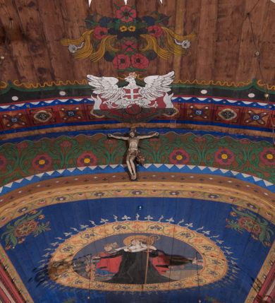 Zdjęcie nr 7: Polichromia o charakterze figuralnym i geometryczno-roślinnym pokrywa ściany i sklepienia prezbiterium, nawy, zakrystii i kruchty zachodniej. Wszystkie ściany prezbiterium do wysokości gzymsu dekorowane są pionowymi, układającymi się naprzemiennie pasami ornamentu roślinno-geometrycznego. Jeden z nich jest granatowy o motywie złotych liści dębu układających się w rozetę z ornamentem geometrycznym. Drugi pas jest żółty z motywem stylizowanych fioletowych i różowych kwiatów o zgeometryzowanych detalach. Gzyms prezbiterium i nawy w kolorze czerwonym, na nim złoty geometryczny pas oraz ornament z granatowych falistych linii wypełnionych w środku białymi punktami. 
Sklepienie prezbiterium jest niebieskie, obramione żółtym pasem z zieloną wicią roślinną, na której ułożone są naprzemiennie granatowe i różowe kwiaty. W narożach stylizowane bukiety kwiatów w kolorach zieleni, brązu i żółci. W centrum sklepienia okrągły medalion ze św. Kingą i Bolesławem Wstydliwym na tle pejzażu wielickiego z kościołem i zamkiem żupnym w oddali. Na pierwszym planie św. Kinga zwrócona jest w swoją prawą stronę, z uniesioną głową. W lewej ręce trzyma pastorał, w prawej wyciągniętej pierścień. Święta ubrana jest w czarny habit klaryski ze szkaplerzem, białą podwiką i welonem oraz czarnym płaszczem z czerwoną podszewką. Na piersi ma złoty łańcuch, na głowie mitrę książęcą. Po prawej stronie św. Kingi klęczy Bolesław Wstydliwy, który obiema rękami trzyma przy rękojeści wbity w ziemię miecz, opleciony skórzanym pasem. Książę ubrany jest w zbroję, niebieską tunikę i czerwony płaszcz spięty złotą fibulą. Na głowie ma kaptur kolczy i hełm z otwartą koroną. Medalion ze sceną ujęty jest żółtą ramą wypełnioną stylizowaną wicią roślinną z naprzemiennie występującymi granatowymi i różowymi kwiatami. Krawędź zewnętrza ozdobiona srebrzystym wieńcem z naprzemiennie ułożonego trójliścia i płomyka. 
Wszystkie ściany nawy pokryte są stylizowanym ornamentem roślinnym składającym się z zielonej wici roślinnej układającej się w regularne medaliony, w których znajdują się kwiaty czerwonego maku. 
Na ścianie północnej w dolnym pasie, pod oknem sześć ostrołukowych arkad na stylizowanych kolumienkach. W pierwszej arkadzie od strony prezbiterium postać klęczącej zakonnicy z opuszczonymi, splecionymi dłońmi, która ubrana jest w biały habit norbertański ze szkaplerzem i brązowy płaszcz z kapturem. U dołu w żółtym polu napis „S(wię)ta BRONISŁAWA”. W drugiej arkadzie królewicz klęczący przy pulpicie, zwrócony w stronę prezbiterium, w obszernym czerwonym płaszczu podbitym futrem i mitrze na głowie. U dołu w żółtym polu napis „S(wię)ty KAZIMIERZ Królewic(z)” W trzeciej arkadzie zwrócona frontalnie siedząca postać z pochyloną głową, ubrana w biały habit zakonny z czarnym płaszczem. U dołu w żółtym polu napis „Bł(ogosławiona) SALOMEA”. W następnych dwóch arkadach występuje stylizowany ornament roślinny z czterema rozetami i ze srebrnym orłem z dwiema tarczami herbowymi, pierwsza z krzyżem na piersi, druga z herbem Szreniawa poniżej. Pole szóstej arkady bez dekoracji. 
Na ścianie południowej w dolnym pasie, pod oknem trzy analogiczne arkady. W pierwszej arkadzie od strony prezbiterium frontalnie siedząca postać w stroju biskupa: białej albie, ciemnoróżowej komży z żółtą lamówką, żółtej kapie i paliuszu, na głowie ma infułę. U dołu w żółtym polu napis „Bł(ogosławiony) WINC(ENTY) KADŁUBEK”. W drugiej arkadzie  postać ukazana w pozycji stojącej, zwróconej w stronę prezbiterium, w prawej ręce trzyma pastorał, lewa w geście błogosławieństwa, ubrana w analogiczny jak poprzednia strój biskupi. U dołu w żółtym polu napis „S(wię)ty STANISŁAW SZCZEP(ANOWSKI)”. W trzeciej arkadzie frontalnie siedząca postać w stroju biskupa: ciemnoróżowej albie, żółtym ornacie, paliuszu, na głowie ma infułę. W  prawej ręce trzyma pastorał, w lewej miniaturę kościoła Mariackiego w Krakowie. Pod nim napis „Bł(ogosławiony) IVO ODROWĄŻ”. 
Sklepienie nawy ujęte ramą złożoną z kilku pasów. Zewnętrzny podzielony na kwadratowe pola, w których naprzemiennie występują dekoracyjny krzyż z kaboszonami i splecionymi literami „MS” oraz wpisany w koło czworoliść z trzema kilofami. Wewnętrzny pas jest zielony dekorowany srebrzonymi kołami, wydzielony zieloną i żółtą falowaną wstęgą. Pośrodku wschodniego pasa obramienia, przy łuku tęczowym znajduje się srebrzony orzeł z tarczą herbową z krzyżem na piersi i tarczą z herbem Szreniawa u dołu. W szponach trzyma trzy kilofy oraz wagę. U dołu znajduje się wstęga z napisem „Arma regiae liberae montanaequae / civitatis Vielicensis”. 
W centrum sklepienia nawy medalion ujęty zewnętrzną ramą utworzoną z grotów i płomieni oraz wewnętrzną z przeplatających się spiralnie wici roślinnych. W polu przedstawienie męczeństwa św. Sebastiana. Postać zwrócona w trzech czwartych w lewo, o bezwładnie opadającym ciele przywiązanym za ramiona i ugięte nogi do drzewa. Wokół głowy nimb zamknięty. Święty przesłonięty w partii podbrzusza białą draperią opadającą na ziemię, po bokach postaci. Ciało wychudzone, o podkreślonej muskulaturze, ze strzałą wbitą w pierś. Święty ukazany na tle lasu, w nocy. W narożach i na osiach sklepienia nawy bukiety kwiatów utworzonych z maków, habrów, kaczeńców i kłosów zbóż. 
W zakrystii na sklepieniu niewielkie Oko Opatrzności w glorii promienistej oraz falista bordiura. Analogiczna bordiura w kruchcie zachodniej. W południowo-zachodnim narożu kruchty północnej malowany na czarno krzyż oraz obok wyryty w drewnie napis: „BI 1898”. W dolnej partii ściany północnej przy chórze muzycznym sygnatura „Włodzimierz Tetmajer pinxit. A(NNO) D(OMINI) MCMVI.”