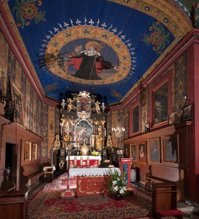 Zdjęcie nr 3: Polichromia o charakterze figuralnym i geometryczno-roślinnym pokrywa ściany i sklepienia prezbiterium, nawy, zakrystii i kruchty zachodniej. Wszystkie ściany prezbiterium do wysokości gzymsu dekorowane są pionowymi, układającymi się naprzemiennie pasami ornamentu roślinno-geometrycznego. Jeden z nich jest granatowy o motywie złotych liści dębu układających się w rozetę z ornamentem geometrycznym. Drugi pas jest żółty z motywem stylizowanych fioletowych i różowych kwiatów o zgeometryzowanych detalach. Gzyms prezbiterium i nawy w kolorze czerwonym, na nim złoty geometryczny pas oraz ornament z granatowych falistych linii wypełnionych w środku białymi punktami. 
Sklepienie prezbiterium jest niebieskie, obramione żółtym pasem z zieloną wicią roślinną, na której ułożone są naprzemiennie granatowe i różowe kwiaty. W narożach stylizowane bukiety kwiatów w kolorach zieleni, brązu i żółci. W centrum sklepienia okrągły medalion ze św. Kingą i Bolesławem Wstydliwym na tle pejzażu wielickiego z kościołem i zamkiem żupnym w oddali. Na pierwszym planie św. Kinga zwrócona jest w swoją prawą stronę, z uniesioną głową. W lewej ręce trzyma pastorał, w prawej wyciągniętej pierścień. Święta ubrana jest w czarny habit klaryski ze szkaplerzem, białą podwiką i welonem oraz czarnym płaszczem z czerwoną podszewką. Na piersi ma złoty łańcuch, na głowie mitrę książęcą. Po prawej stronie św. Kingi klęczy Bolesław Wstydliwy, który obiema rękami trzyma przy rękojeści wbity w ziemię miecz, opleciony skórzanym pasem. Książę ubrany jest w zbroję, niebieską tunikę i czerwony płaszcz spięty złotą fibulą. Na głowie ma kaptur kolczy i hełm z otwartą koroną. Medalion ze sceną ujęty jest żółtą ramą wypełnioną stylizowaną wicią roślinną z naprzemiennie występującymi granatowymi i różowymi kwiatami. Krawędź zewnętrza ozdobiona srebrzystym wieńcem z naprzemiennie ułożonego trójliścia i płomyka. 
Wszystkie ściany nawy pokryte są stylizowanym ornamentem roślinnym składającym się z zielonej wici roślinnej układającej się w regularne medaliony, w których znajdują się kwiaty czerwonego maku. 
Na ścianie północnej w dolnym pasie, pod oknem sześć ostrołukowych arkad na stylizowanych kolumienkach. W pierwszej arkadzie od strony prezbiterium postać klęczącej zakonnicy z opuszczonymi, splecionymi dłońmi, która ubrana jest w biały habit norbertański ze szkaplerzem i brązowy płaszcz z kapturem. U dołu w żółtym polu napis „S(wię)ta BRONISŁAWA”. W drugiej arkadzie królewicz klęczący przy pulpicie, zwrócony w stronę prezbiterium, w obszernym czerwonym płaszczu podbitym futrem i mitrze na głowie. U dołu w żółtym polu napis „S(wię)ty KAZIMIERZ Królewic(z)” W trzeciej arkadzie zwrócona frontalnie siedząca postać z pochyloną głową, ubrana w biały habit zakonny z czarnym płaszczem. U dołu w żółtym polu napis „Bł(ogosławiona) SALOMEA”. W następnych dwóch arkadach występuje stylizowany ornament roślinny z czterema rozetami i ze srebrnym orłem z dwiema tarczami herbowymi, pierwsza z krzyżem na piersi, druga z herbem Szreniawa poniżej. Pole szóstej arkady bez dekoracji. 
Na ścianie południowej w dolnym pasie, pod oknem trzy analogiczne arkady. W pierwszej arkadzie od strony prezbiterium frontalnie siedząca postać w stroju biskupa: białej albie, ciemnoróżowej komży z żółtą lamówką, żółtej kapie i paliuszu, na głowie ma infułę. U dołu w żółtym polu napis „Bł(ogosławiony) WINC(ENTY) KADŁUBEK”. W drugiej arkadzie  postać ukazana w pozycji stojącej, zwróconej w stronę prezbiterium, w prawej ręce trzyma pastorał, lewa w geście błogosławieństwa, ubrana w analogiczny jak poprzednia strój biskupi. U dołu w żółtym polu napis „S(wię)ty STANISŁAW SZCZEP(ANOWSKI)”. W trzeciej arkadzie frontalnie siedząca postać w stroju biskupa: ciemnoróżowej albie, żółtym ornacie, paliuszu, na głowie ma infułę. W  prawej ręce trzyma pastorał, w lewej miniaturę kościoła Mariackiego w Krakowie. Pod nim napis „Bł(ogosławiony) IVO ODROWĄŻ”. 
Sklepienie nawy ujęte ramą złożoną z kilku pasów. Zewnętrzny podzielony na kwadratowe pola, w których naprzemiennie występują dekoracyjny krzyż z kaboszonami i splecionymi literami „MS” oraz wpisany w koło czworoliść z trzema kilofami. Wewnętrzny pas jest zielony dekorowany srebrzonymi kołami, wydzielony zieloną i żółtą falowaną wstęgą. Pośrodku wschodniego pasa obramienia, przy łuku tęczowym znajduje się srebrzony orzeł z tarczą herbową z krzyżem na piersi i tarczą z herbem Szreniawa u dołu. W szponach trzyma trzy kilofy oraz wagę. U dołu znajduje się wstęga z napisem „Arma regiae liberae montanaequae / civitatis Vielicensis”. 
W centrum sklepienia nawy medalion ujęty zewnętrzną ramą utworzoną z grotów i płomieni oraz wewnętrzną z przeplatających się spiralnie wici roślinnych. W polu przedstawienie męczeństwa św. Sebastiana. Postać zwrócona w trzech czwartych w lewo, o bezwładnie opadającym ciele przywiązanym za ramiona i ugięte nogi do drzewa. Wokół głowy nimb zamknięty. Święty przesłonięty w partii podbrzusza białą draperią opadającą na ziemię, po bokach postaci. Ciało wychudzone, o podkreślonej muskulaturze, ze strzałą wbitą w pierś. Święty ukazany na tle lasu, w nocy. W narożach i na osiach sklepienia nawy bukiety kwiatów utworzonych z maków, habrów, kaczeńców i kłosów zbóż. 
W zakrystii na sklepieniu niewielkie Oko Opatrzności w glorii promienistej oraz falista bordiura. Analogiczna bordiura w kruchcie zachodniej. W południowo-zachodnim narożu kruchty północnej malowany na czarno krzyż oraz obok wyryty w drewnie napis: „BI 1898”. W dolnej partii ściany północnej przy chórze muzycznym sygnatura „Włodzimierz Tetmajer pinxit. A(NNO) D(OMINI) MCMVI.”