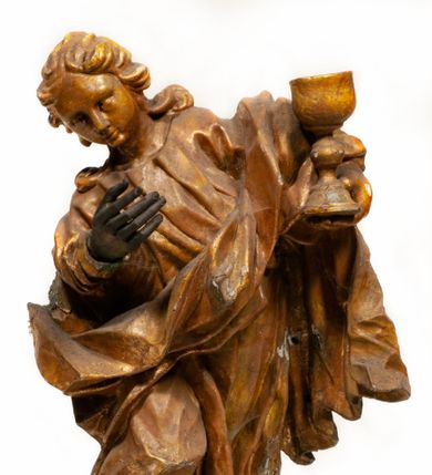 Zdjęcie nr 1: Rzeźba pełnoplastyczna, zwrócona frontalnie, ukazana w silnym kontrapoście i przegięciu ciała w prawą stronę. Święty lewą ręką podtrzymuje kielich, prawą wyciąga do przodu. Jego twarz jest okrągła o pełnych policzkach, okrągłych oczach, małym, prostym nosie, pełnych ustach i wystającej brodzie. Okolona jest długimi, silnie kręconymi włosami, opadającymi skręconymi pasmami na ramiona. Święty ubrany jest w obficie drapowaną tunikę, przylegającą do ciała w partii nóg oraz płaszcz zarzucony na plecy, z przodu postaci skręcony i zarzucony na lewe przedramię. Figura w całości pozłocona. 

