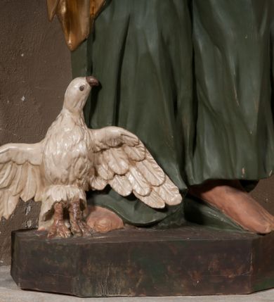 Zdjęcie nr 4: Rzeźba drążona, postać umieszczona na cokole. Święty Jan Ewangelista ukazany w całej postaci, frontalnie, prawą rękę przyciska do piersi w lewej opuszczonej wzdłuż ciała trzyma zamkniętą księgę. Twarz pociągła, o pełnych policzkach z długim nosem, małymi ustami oraz jasnoniebieskimi oczami, okolona krótkimi brązowymi włosami układającymi się w pukle. Święty jest ubrany w zieloną tunikę z wąskimi rękawami opadającą do podstawy płytkimi, miękkimi fałdami oraz złoty płaszcz spięty na dekolcie, zarzucony na ramiona, podtrzymywany z przodu przez prawe przedramię. Obok bosych stóp świętego, po jego prawej stronie ukazany biały orzeł z rozpostartymi skrzydłami.