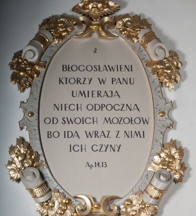 Zdjęcie nr 4: Rzeźba drążona, postać umieszczona na cokole, przedstawiająca św. Łukasza Ewangelistę. Święty ukazany jest w pozycji stojącej, z górną partią ciała skręconą nieznacznie w lewo, z lekko pochyloną głową. Ręce ma ugięte, w lewej trzyma otwartą księgę, prawą wyciąga przed siebie. Ma pociągłą twarz z okrągłymi oczami, długim nosem i wydatnymi ustami, okoloną krótkimi, opadającymi do tyłu puklami włosów oraz długą, dzielącą się na końcu w dwa pukle brodę. Święty odziany jest w przewiązaną w pasie niebieską suknię opadającą do stóp płytkimi, miękkimi fałdami oraz złoty płaszcz, zarzucony na ramiona i otaczający biodra, przytrzymany z przodu rękami, układający się w głębokie, nieregularne fałdy. U bosych stóp świętego wół.