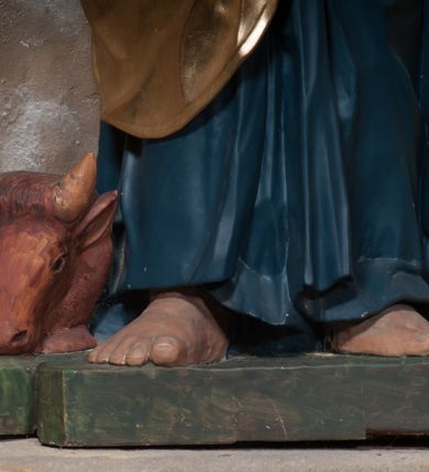 Zdjęcie nr 2: Rzeźba drążona, postać umieszczona na cokole, przedstawiająca św. Łukasza Ewangelistę. Święty ukazany jest w pozycji stojącej, z górną partią ciała skręconą nieznacznie w lewo, z lekko pochyloną głową. Ręce ma ugięte, w lewej trzyma otwartą księgę, prawą wyciąga przed siebie. Ma pociągłą twarz z okrągłymi oczami, długim nosem i wydatnymi ustami, okoloną krótkimi, opadającymi do tyłu puklami włosów oraz długą, dzielącą się na końcu w dwa pukle brodę. Święty odziany jest w przewiązaną w pasie niebieską suknię opadającą do stóp płytkimi, miękkimi fałdami oraz złoty płaszcz, zarzucony na ramiona i otaczający biodra, przytrzymany z przodu rękami, układający się w głębokie, nieregularne fałdy. U bosych stóp świętego wół.