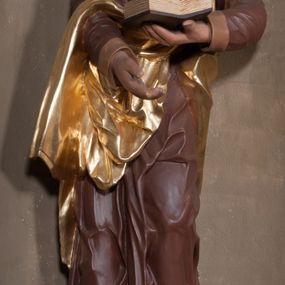 Zdjęcie nr 1: Rzeźba drążona, postać umieszczona na cokole przedstawiająca św. Marka Ewangelistę. Święty ukazany jest w pozycji stojącej, w kontrapoście, z lewą nogą zgiętą w kolanie i sylwetką przechyloną nieznacznie na lewą stronę, a głową odwróconą w przeciwnym kierunku. Prawa ręka wyprostowana, wyciągnięta przed siebie, lewa ugięta, podtrzymuje otwartą księgę. Święty ma pociągłą twarz o okrągłych, szeroko otwartych, niebieskich oczach, długim, wąskim nosie i małych ustach, okoloną zwiniętymi w pukle włosami zakrywającymi uszy oraz od dołu silnie poskręcaną brodę. Ubrany jest w brązową suknię z podwiniętymi rękawami opadającą do stóp podkreślającymi anatomię fałdami oraz w złoty płaszcz przechodzący przez lewy bark i zarzucony na prawe przedramię, układający się w nieregularne, głębokie fałdy. Stopy bose. Przy prawej nodze świętego lew. 