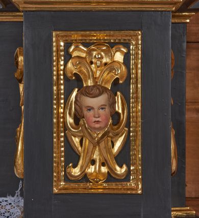 Zdjęcie nr 5: Nastawa architektoniczna, jednoosiowa, jednokondygnacyjna. Ołtarz drewniany, sarkofagowy z drewnianą mensą, od frontu dekorowany malowanym na złoto medalionem złożonym z czterech spiętych kabłąkami wolutek. Całość obwiedziona malowaną w kolorze złotym, cienką ramką z wolutkami w narożach. Na mensie ustawione jest nowe tabernakulum w formie prostopadłościennej skrzynki. Ścianki tabernakulum ujęte są złoconymi listewkami, zdobionymi wicią roślinną; drzwiczki w kształcie stojącego prostokąta z płaskorzeźbionym przedstawieniem kielicha z hostią w polu oraz winnym gronem i kłosami zboża po bokach na srebrnym tle. Nastawa ustawiona na cokole, ujęta parą złoconych, gładkich kolumn, dźwigających przerwane belkowanie. Kolumny ustawione są na cokołach wysuniętych przed lico ołtarza, za nimi dekoracja małżowinowo-chrząstkowa, kapitele kompozytowe. Cokoły zdobione są prostokątnymi płycinami zdobionymi na ściankach bocznych ornamentem małżowinowo-chrząstkowym, a na ściankach frontowych główkami aniołków na tle ornamentu. Twarze aniołków o pucułowatych policzkach i bujnych włosach, skierowane na wprost, z chustami pod szyją. W predelli znajduje się płycina w kształcie leżącego prostokąta o półkoliście zakończonych bokach. W polu środkowym nastawy obraz św. Otylii w formie stojącego prostokąta ujęty szeroką ramą, zdobioną ornamentem małżowinowo-chrząstkowym. Całość zamknięta jest przerywanym trójkątnym przyczółkiem. Pośrodku przyczółka pole zamknięte łukiem półkolistym. Kondygnacja ujęta jest po bokach uszami z ornamentu małżowinowo-chrząstkowego. Struktura polichromowana na czarno, profilowania i ornamentyka złocone. 
