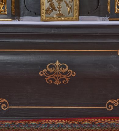 Zdjęcie nr 7: Nastawa architektoniczna, jednoosiowa, jednokondygnacyjna. Ołtarz drewniany, sarkofagowy z drewnianą mensą, od frontu dekorowany malowanym na złoto medalionem złożonym z czterech spiętych kabłąkami wolutek. Całość obwiedziona malowaną w kolorze złotym, cienką ramką z wolutkami w narożach. Na mensie ustawione jest nowe tabernakulum w formie prostopadłościennej skrzynki. Ścianki tabernakulum ujęte są złoconymi listewkami, zdobionymi wicią roślinną; drzwiczki w kształcie stojącego prostokąta z płaskorzeźbionym przedstawieniem kielicha z hostią w polu oraz winnym gronem i kłosami zboża po bokach na srebrnym tle. Nastawa ustawiona na cokole, ujęta parą złoconych, gładkich kolumn, dźwigających przerwane belkowanie. Kolumny ustawione są na cokołach wysuniętych przed lico ołtarza, za nimi dekoracja małżowinowo-chrząstkowa, kapitele kompozytowe. Cokoły zdobione są prostokątnymi płycinami zdobionymi na ściankach bocznych ornamentem małżowinowo-chrząstkowym, a na ściankach frontowych główkami aniołków na tle ornamentu. Twarze aniołków o pucułowatych policzkach i bujnych włosach, skierowane na wprost, z chustami pod szyją. W predelli znajduje się płycina w kształcie leżącego prostokąta o półkoliście zakończonych bokach. W polu środkowym nastawy obraz św. Otylii w formie stojącego prostokąta ujęty szeroką ramą, zdobioną ornamentem małżowinowo-chrząstkowym. Całość zamknięta jest przerywanym trójkątnym przyczółkiem. Pośrodku przyczółka pole zamknięte łukiem półkolistym. Kondygnacja ujęta jest po bokach uszami z ornamentu małżowinowo-chrząstkowego. Struktura polichromowana na czarno, profilowania i ornamentyka złocone. 
