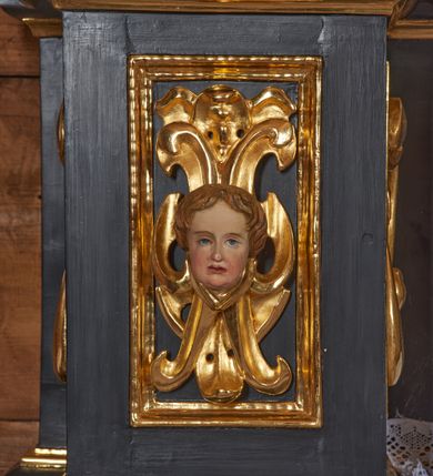 Zdjęcie nr 6: Nastawa architektoniczna, jednoosiowa, jednokondygnacyjna. Ołtarz drewniany, sarkofagowy z drewnianą mensą, od frontu dekorowany malowanym na złoto medalionem złożonym z czterech spiętych kabłąkami wolutek. Całość obwiedziona malowaną w kolorze złotym, cienką ramką z wolutkami w narożach. Na mensie ustawione jest nowe tabernakulum w formie prostopadłościennej skrzynki. Ścianki tabernakulum ujęte są złoconymi listewkami, zdobionymi wicią roślinną; drzwiczki w kształcie stojącego prostokąta z płaskorzeźbionym przedstawieniem kielicha z hostią w polu oraz winnym gronem i kłosami zboża po bokach na srebrnym tle. Nastawa ustawiona na cokole, ujęta parą złoconych, gładkich kolumn, dźwigających przerwane belkowanie. Kolumny ustawione są na cokołach wysuniętych przed lico ołtarza, za nimi dekoracja małżowinowo-chrząstkowa, kapitele kompozytowe. Cokoły zdobione są prostokątnymi płycinami zdobionymi na ściankach bocznych ornamentem małżowinowo-chrząstkowym, a na ściankach frontowych główkami aniołków na tle ornamentu. Twarze aniołków o pucułowatych policzkach i bujnych włosach, skierowane na wprost, z chustami pod szyją. W predelli znajduje się płycina w kształcie leżącego prostokąta o półkoliście zakończonych bokach. W polu środkowym nastawy obraz św. Otylii w formie stojącego prostokąta ujęty szeroką ramą, zdobioną ornamentem małżowinowo-chrząstkowym. Całość zamknięta jest przerywanym trójkątnym przyczółkiem. Pośrodku przyczółka pole zamknięte łukiem półkolistym. Kondygnacja ujęta jest po bokach uszami z ornamentu małżowinowo-chrząstkowego. Struktura polichromowana na czarno, profilowania i ornamentyka złocone. 
