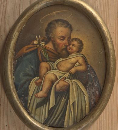 Zdjęcie nr 1: Obraz w kształcie owalu przedstawiający św. Józefa z Dzieciątkiem. Święty został ukazany w popiersiu, delikatnie zwrócony w lewo. Na rękach trzyma Dzieciątko Jezus oraz gałązkę białej lilii, która opiera się o jego prawe ramię. Święty ubrany jest w niebieską szatę z długimi rękawami oraz brązowy płaszcz spięty na prawym ramieniu broszą. Ma podłużną twarz okoloną krótką brodą, jasnobrązowe i kędzierzawe włosy, długi i wąski nos oraz delikatnie przymknięte oczy ze wzrokiem wpatrzonym w Jezusa. Dzieciątko ułożone jest w pozycji półleżącej na lewym ręku św. Józefa z uniesioną prawą nóżką i lewą rączką ugiętą w łokciu. Jezus ubrany jest w jasną pieluszkę, odsłaniającą lewą rączkę oraz tors i obficie spływającą w dół. Ma twarz o rysach niemowlęcych z pulchnymi i zarumienionymi policzkami. Wokół głowy Dzieciątka namalowany jest delikatny i promienisty nimb, a nad głową św. Józefa znajduje się nimb okrągły. Całość ukazana jest na ugrowym tle. Rama drewniana, okrągła, złocona.
