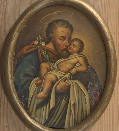 Zdjęcie nr 1: Obraz w kształcie owalu przedstawiający św. Józefa z Dzieciątkiem. Święty został ukazany w popiersiu, delikatnie zwrócony w lewo. Na rękach trzyma Dzieciątko Jezus oraz gałązkę białej lilii, która opiera się o jego prawe ramię. Święty ubrany jest w niebieską szatę z długimi rękawami oraz brązowy płaszcz spięty na prawym ramieniu broszą. Ma podłużną twarz okoloną krótką brodą, jasnobrązowe i kędzierzawe włosy, długi i wąski nos oraz delikatnie przymknięte oczy ze wzrokiem wpatrzonym w Jezusa. Dzieciątko ułożone jest w pozycji półleżącej na lewym ręku św. Józefa z uniesioną prawą nóżką i lewą rączką ugiętą w łokciu. Jezus ubrany jest w jasną pieluszkę, odsłaniającą lewą rączkę oraz tors i obficie spływającą w dół. Ma twarz o rysach niemowlęcych z pulchnymi i zarumienionymi policzkami. Wokół głowy Dzieciątka namalowany jest delikatny i promienisty nimb, a nad głową św. Józefa znajduje się nimb okrągły. Całość ukazana jest na ugrowym tle. Rama drewniana, okrągła, złocona.
