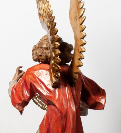 Zdjęcie nr 16: Tabernakulum proste, w formie prostopadłościennej skrzynki, o złotych drzwiczkach z wytłaczaną formą równoramiennego krzyża i wypukłą srebrną rybą oraz koszem z chlebem pośrodku. Po obu stronach, na niewysokich postumentach umieszczone dwa klęczące anioły z wysokimi, uniesionymi do góry skrzydłami, zwróconymi ku środkowi. Twarze o delikatnych rysach, silnie zarumienionych policzkach z 
długimi nosami, głęboko osadzonymi oczami i wysuniętym podbródkiem. Włosy długie, bujne, skręcone w duże pukle po bokach głowy. Anioły ubrane są w białe suknie i czerwone dalmatyki o fioletowych podszewkach. Anioł po lewej stronie trzyma w dłoniach kadzielnicę, a anioł po prawej płomienisty wazon. Polichromie w odsłoniętych partiach ciała naturalistyczne. 


