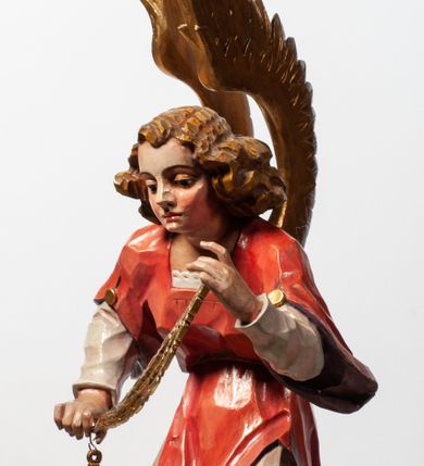 Zdjęcie nr 19: Tabernakulum proste, w formie prostopadłościennej skrzynki, o złotych drzwiczkach z wytłaczaną formą równoramiennego krzyża i wypukłą srebrną rybą oraz koszem z chlebem pośrodku. Po obu stronach, na niewysokich postumentach umieszczone dwa klęczące anioły z wysokimi, uniesionymi do góry skrzydłami, zwróconymi ku środkowi. Twarze o delikatnych rysach, silnie zarumienionych policzkach z 
długimi nosami, głęboko osadzonymi oczami i wysuniętym podbródkiem. Włosy długie, bujne, skręcone w duże pukle po bokach głowy. Anioły ubrane są w białe suknie i czerwone dalmatyki o fioletowych podszewkach. Anioł po lewej stronie trzyma w dłoniach kadzielnicę, a anioł po prawej płomienisty wazon. Polichromie w odsłoniętych partiach ciała naturalistyczne. 


