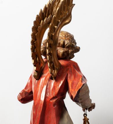 Zdjęcie nr 17: Tabernakulum proste, w formie prostopadłościennej skrzynki, o złotych drzwiczkach z wytłaczaną formą równoramiennego krzyża i wypukłą srebrną rybą oraz koszem z chlebem pośrodku. Po obu stronach, na niewysokich postumentach umieszczone dwa klęczące anioły z wysokimi, uniesionymi do góry skrzydłami, zwróconymi ku środkowi. Twarze o delikatnych rysach, silnie zarumienionych policzkach z 
długimi nosami, głęboko osadzonymi oczami i wysuniętym podbródkiem. Włosy długie, bujne, skręcone w duże pukle po bokach głowy. Anioły ubrane są w białe suknie i czerwone dalmatyki o fioletowych podszewkach. Anioł po lewej stronie trzyma w dłoniach kadzielnicę, a anioł po prawej płomienisty wazon. Polichromie w odsłoniętych partiach ciała naturalistyczne. 


