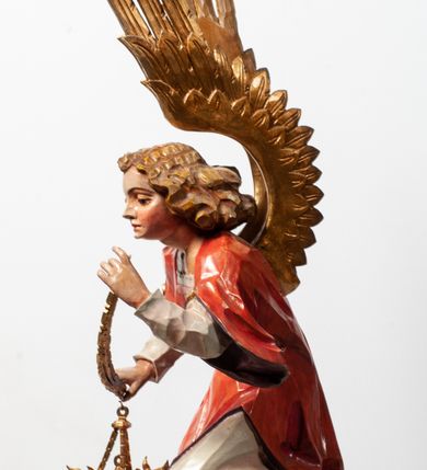 Zdjęcie nr 20: Tabernakulum proste, w formie prostopadłościennej skrzynki, o złotych drzwiczkach z wytłaczaną formą równoramiennego krzyża i wypukłą srebrną rybą oraz koszem z chlebem pośrodku. Po obu stronach, na niewysokich postumentach umieszczone dwa klęczące anioły z wysokimi, uniesionymi do góry skrzydłami, zwróconymi ku środkowi. Twarze o delikatnych rysach, silnie zarumienionych policzkach z 
długimi nosami, głęboko osadzonymi oczami i wysuniętym podbródkiem. Włosy długie, bujne, skręcone w duże pukle po bokach głowy. Anioły ubrane są w białe suknie i czerwone dalmatyki o fioletowych podszewkach. Anioł po lewej stronie trzyma w dłoniach kadzielnicę, a anioł po prawej płomienisty wazon. Polichromie w odsłoniętych partiach ciała naturalistyczne. 


