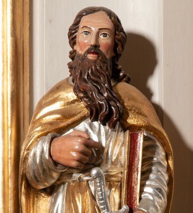 Zdjęcie nr 1: Święty Paweł ukazany całopostaciowo, frontalnie. W lewej dłoni trzyma miecz, ostrzem skierowany w dół, prawą ugiętą w łokciu, składa na piersi. Pod lewą ręką trzyma zamkniętą księgę. Twarz szeroka, nos długi, okolona długimi, pofalowanymi, brązowymi włosami i długą, brązową brodą. Ubrany jest w długą, srebrną suknię i złoty, pofałdowany, spięty na piersi płaszcz. Polichromia w odsłoniętych partiach ciała naturalistyczna, szaty i atrybuty złocone i srebrzone.