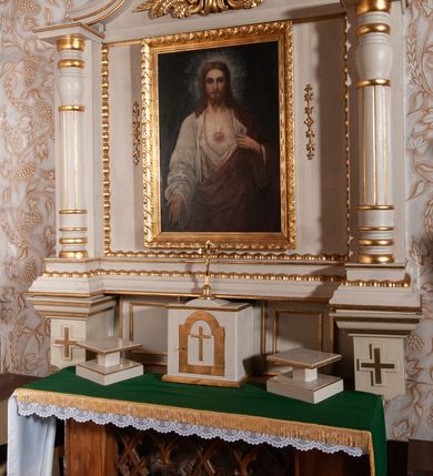 Zdjęcie nr 6: Ołtarz architektoniczny, jednokondygnacyjny, jednoosiowy. Ołtarz flankowany dwoma filarami na niskich cokołach, pośrodku ażurowa, neogotycka krata; mensa drewniana. Tabernakulum w formie prostopadłościennej skrzynki, ustawione na niskim cokole. Na ściance przedniej drzwiczki w kształcie stojącego prostokąta, zamkniętego łukiem nadwieszonym. W polu w płycinie o analogicznym kształcie łaciński krzyżyk. Na tabernakulum niska kopuła, a na niej ustawiony niewielki krucyfiks. Nastawa ustawiona na niskim cokole o wysuniętych po bokach impostach zdobionych greckimi krzyżykami. Kondygnacja ujęta parą kolumn, w dolnej części złożoną z profilowanych talerzyków, powyżej o kanelowanym trzonie, a w górnej części o gruszkowej formie zamkniętej talerzykami. Podpory wspierają przerywany nad polem środkowym gzyms. Całość zamyka para spływów wolutowych z krzyżykiem pośrodku. W polu głównym obraz Najświętsze Serce Jezusa, po bokach flankowany zwisami kwiatów, powyżej rzeźbioną dekoracją zawiniętych wolutowo liści akantu. Wzdłuż podstawy retabulum oraz wokół pola środkowego przebiega złocony, rzeźbiony kimation. Struktura polichromowana w kolorze beżowy, detale i ornamentyka złocone.

