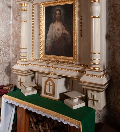 Zdjęcie nr 5: Ołtarz architektoniczny, jednokondygnacyjny, jednoosiowy. Ołtarz flankowany dwoma filarami na niskich cokołach, pośrodku ażurowa, neogotycka krata; mensa drewniana. Tabernakulum w formie prostopadłościennej skrzynki, ustawione na niskim cokole. Na ściance przedniej drzwiczki w kształcie stojącego prostokąta, zamkniętego łukiem nadwieszonym. W polu w płycinie o analogicznym kształcie łaciński krzyżyk. Na tabernakulum niska kopuła, a na niej ustawiony niewielki krucyfiks. Nastawa ustawiona na niskim cokole o wysuniętych po bokach impostach zdobionych greckimi krzyżykami. Kondygnacja ujęta parą kolumn, w dolnej części złożoną z profilowanych talerzyków, powyżej o kanelowanym trzonie, a w górnej części o gruszkowej formie zamkniętej talerzykami. Podpory wspierają przerywany nad polem środkowym gzyms. Całość zamyka para spływów wolutowych z krzyżykiem pośrodku. W polu głównym obraz Najświętsze Serce Jezusa, po bokach flankowany zwisami kwiatów, powyżej rzeźbioną dekoracją zawiniętych wolutowo liści akantu. Wzdłuż podstawy retabulum oraz wokół pola środkowego przebiega złocony, rzeźbiony kimation. Struktura polichromowana w kolorze beżowy, detale i ornamentyka złocone.

