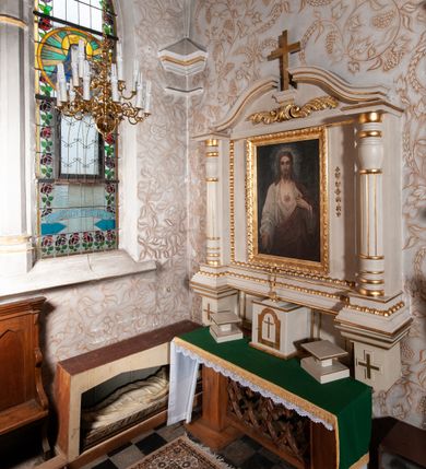 Zdjęcie nr 4: Ołtarz architektoniczny, jednokondygnacyjny, jednoosiowy. Ołtarz flankowany dwoma filarami na niskich cokołach, pośrodku ażurowa, neogotycka krata; mensa drewniana. Tabernakulum w formie prostopadłościennej skrzynki, ustawione na niskim cokole. Na ściance przedniej drzwiczki w kształcie stojącego prostokąta, zamkniętego łukiem nadwieszonym. W polu w płycinie o analogicznym kształcie łaciński krzyżyk. Na tabernakulum niska kopuła, a na niej ustawiony niewielki krucyfiks. Nastawa ustawiona na niskim cokole o wysuniętych po bokach impostach zdobionych greckimi krzyżykami. Kondygnacja ujęta parą kolumn, w dolnej części złożoną z profilowanych talerzyków, powyżej o kanelowanym trzonie, a w górnej części o gruszkowej formie zamkniętej talerzykami. Podpory wspierają przerywany nad polem środkowym gzyms. Całość zamyka para spływów wolutowych z krzyżykiem pośrodku. W polu głównym obraz Najświętsze Serce Jezusa, po bokach flankowany zwisami kwiatów, powyżej rzeźbioną dekoracją zawiniętych wolutowo liści akantu. Wzdłuż podstawy retabulum oraz wokół pola środkowego przebiega złocony, rzeźbiony kimation. Struktura polichromowana w kolorze beżowy, detale i ornamentyka złocone.

