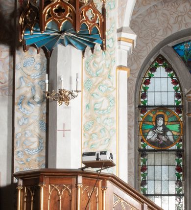 Zdjęcie nr 1: Ambona stojąca, przyścienna, usytuowana przy ścianie północnej, pomiędzy pierwszym a drugim przęsłem nawy. Ustawiona na wysokim, sześciobocznym dwukondygnacyjnym filarze na wysokim cokole. Filar artykułowany smukłymi, złoconymi kolumienkami o jońskich kapitelach. W polach pomiędzy nimi płyciny zamknięte ostrołukowo. Kosz sześcioboczny o stożkowatej podstawie zamkniętej profilowanym gzymsem. Ścianki rozczłonkowane za pomocą analogicznych jak wcześniej kolumienek; w polach prostokątne płyciny, w których przecinające się, złocone arkadki. Całość zamyka profilowany parapet. Baldachim na planie analogicznym do kosza, węższy od niego, od dołu ujęty krenelażem, od góry rzeźbionym, ażurowym ornamentem ze spiętych arkadek, oddzielonych niewielkimi pinaklami. Całość zamknięta architektoniczną strukturą z pinaklem i łacińskim krzyżykiem u szczytu. U podniebienia na niebieskim tle rzeźbiona gołębica Ducha Świętego otoczona promieniami. Na ambonę prowadzą od wschodu, drewniane dwudzielne schody z balustradą dekorowaną analogicznie jak kosz.