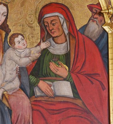 Zdjęcie nr 4: Obraz w kształcie stojącego prostokąta zamkniętego łukiem półkolistym. W centrum kompozycji ukazane frontalnie, siedzące obok siebie Maria trzymająca Dzieciątko na kolanach (z lewej) oraz św. Anna (z prawej). Maria przedstawiona jako młoda kobieta o owalnej twarzy oraz długich, falowanych włosach w kolorze jasnobrązowym, opadających na ramiona. Jej głowa ujęta w trzech czwartych zwrócona jest w kierunku św. Anny i nieznacznie pochylona w dół. Oczy ciemne, wzrok skierowany do dołu, w kierunku Dzieciątka. Nos wydatny, prosty, usta niewielkie, jasnoróżowe. Karnacja postaci jasna z delikatnie zaznaczonymi różem policzkami. Maria ubrana jest w jasnoróżową suknię z długimi rękawami przewiązaną w pasie jasnobrązową szarfą oraz obszerny, niebieski płaszcz z żółtą podszewką. Wokół dekoltu biała chusta. Spod szat widoczna jest stopa obuta w czerwony sandał. Na głowie postaci znajduje się wysadzana kamieniami, złota korona. Wokół głowy nimb zaznaczony w złoconym tle. Dzieciątko zostało ukazane w dynamicznej pozie, klęczy na kolanach Marii, z rękami wyciągniętymi w kierunku św. Anny. Jego okrągła twarz ma jasną karnację z wyraźnie zaznaczonym rumieńcem. Oczy są ciemne, nos prosty, a usta małe. Włosy Dzieciątka są krótkie, jasne i kręcone. Postać ubrana jest w tunikę z długimi rękawami wykonaną z przejrzystej tkaniny. W górnej części kompozycji, w partii tła, wysoko ponad głową Dzieciątka wyryta korona. Święta Anna została przedstawiona jako dojrzała kobieta o wyrazistych rysach twarzy z dużymi, ciemnymi oczami oraz wydatnym nosem. Głowę pochyla w dół, a wzrok zwraca w kierunku Dzieciątka. W swojej lewej dłoni trzyma niewielki kwiat (różę?), prawą podtrzymuje otwartą księgę. Święta ubrana jest w ciemnozieloną suknię z długimi rękawami, wokół szyi oraz na głowie nosi białą chustę, na którą narzucony jest czerwony płaszcz o jasnobrązowej podszewce. Spod szat widoczna jest stopa obuta w czarny trzewik o lekko spiczastym nosku. Wokół głowy świętej zaznaczony w złoconym tle nimb. Na drugim planie, w nieco pomniejszonej skali ukazani zostali św. Józef (z lewej strony obrazu) oraz św. Joachim (z prawej). Święty Józef został przedstawiony jako starszy siwy mężczyzna z włosami przerzedzonymi w okolicach czoła oraz z długą, siwą brodą i wąsami. Oczy duże, ciemne, nos krótki, na czole postaci delikatnie zaznaczone zmarszczki. Postać ubrana w zielone i brązowe szaty. Świętego Joachima ukazano jako starszego mężczyznę o podłużnej twarzy, dużych, ciemnych oczach, wydatnym, prostym nosie z długą, siwą brodą i wąsami. Ubrany jest w granatowe szaty oraz czerwony kapelusz. Tło obrazu złocone, dekorowane rytym ornamentem roślinnym o symetrycznym przebiegu. W dolnej części obrazu, na pierwszym planie przedstawione białe, czerwone oraz niebieskie kwiaty o zielonych łodyżkach ukazane na brązowym tle.