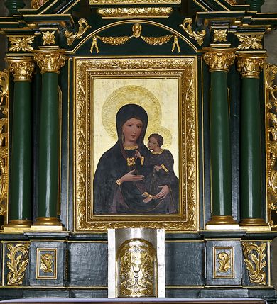 Zdjęcie nr 7: Obraz w kształcie stojącego prostokąta ujęty profilowaną ramą zdobioną akantem. W centrum kompozycji ukazana Matka Boska z Dzieciątkiem w typie Hodegetrii. Maria przedstawiona frontalnie, w popiersiu z głową nieznacznie pochyloną w lewo, w kierunku Dzieciątka, które trzyma na lewym ramieniu. Prawą ręką wskazuje na Jezusa. Twarz Matki Boskiej szczupła, z długim, prostym nosem i niewielkimi ustami. Na policzkach zaznaczony delikatny rumieniec. Wokół głowy złocony nimb z umieszczoną w otoku gotycką inskrypcją: „Regina • celi • letare • alle • quia • quem • meruisti • portare • alle • resurrexit • sicu”. Maria ubrana jest w ciemnogranatową szatę spodnią z długimi rękawami, wykończoną złoconą lamówką. Przy dekolcie gotycki, minuskułowy napis: „ave • maria”. Na ramiona i głowę ma narzucony ciemnogranatowy płaszcz z purpurową podszewką, spięty pod szyją ozdobną, kameryzowaną broszą. Spod płaszcza widoczna przejrzysta chusta oraz jasne, falowane włosy. Dzieciątko Jezus zwrócone w stronę Marii, prawą rękę wyciąga w geście błogosławieństwa, w lewej zaś trzyma zamkniętą księgę w zielonej oprawie. Przedstawione jako brązowooki chłopiec o krótkich, jasnych i kręconych włosach. Dzieciątko ubrane jest w ciemnogranatową tunikę z długimi rękawami zdobioną motywem kwiatowym, wykończoną złotą lamówką. Spod szat widoczne są bose stopy. Wokół głowy Jezusa umieszczony złocony nimb wypełniony rytą dekoracją roślinną. Tło obrazu jednolicie złocone z rytą dekoracją roślinną.