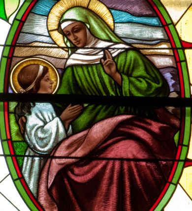 Zdjęcie nr 5: Witraż w kształcie stojącego prostokąta zamkniętego łukiem półkolistym. Kompozycja ujęta geometryczną bordiurą w kolorach czerwonym oraz jasno- i ciemnożółtym. Wewnątrz pole w kształcie stojącego prostokąta zamkniętego łukiem półkolistym z wpisanymi dwoma ostrołukami tworzącymi rodzaj gotyckiego biforium. W jego górnej części motyw kłosów oraz winnych gron. W polu z lewej strony kompozycji owalny medalion mieszczący przedstawienie św. Władysława w rycerskiej zbroi, zielonej tunice ze złotymi lamówkami i królewskim, czerwonym płaszczu z gronostajowym podbiciem umieszczone na tle pejzażu. Święty ukazany w tzw. długim popiersiu z ciałem zwróconym w trzech czwartych w prawo. Prawa ręka złożona na piersi, w lewej tarcza podzielona w słup, po prawej stronie białe i czerwone pasy, po lewej na srebrnym polu złoty krzyż z dwiema belkami. Na głowie hełm z koroną, wokół głowy nimb. Poniżej medalionu czerwona litera „A” w jasnożółtym polu w kształcie rombu oraz inskrypcja: „FUNDACJA / KS(IĄDZ) WŁADYSŁAW ZIEMIŃSKI PROBOSZCZ / R(OKU) P(AŃSKIEGO) 1937”. W polu z prawej strony kompozycji owalny medalion mieszczący scenę Nauczania Marii przez św. Annę umieszczoną na tle pejzażu. Święta Anna ukazana w pozycji siedzącej, z ciałem zwróconym w trzech czwartych w prawo, pochyla się ku stojącej po jej prawej stronie Marii. Lewa dłoń uniesiona w geście nauczania. Anna przedstawiona jako dojrzała kobieta ubrana w zieloną suknię, białą podwikę oraz czerwony płaszcz. Na głowie jasnozielona chusta. Maria ukazana z profilu w pozycji stojącej. Została przedstawiona jako kilkuletnia dziewczyna o długich, brązowych i falowanych włosach ujętych jasną opaską. Wokół głowy nimb. Ręce złożone w geście modlitwy. Postać ubrana jest w jasnoniebieską tunikę. Poniżej medaliony litera „Ω” w jasnożółtym polu w kształcie rombu oraz inskrypcja „FRANASOWA ANNA R(OKU) P(AŃSKIEGO) 1937”. 

