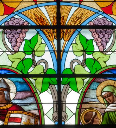 Zdjęcie nr 3: Witraż w kształcie stojącego prostokąta zamkniętego łukiem półkolistym. Kompozycja ujęta geometryczną bordiurą w kolorach czerwonym oraz jasno- i ciemnożółtym. Wewnątrz pole w kształcie stojącego prostokąta zamkniętego łukiem półkolistym z wpisanymi dwoma ostrołukami tworzącymi rodzaj gotyckiego biforium. W jego górnej części motyw kłosów oraz winnych gron. W polu z lewej strony kompozycji owalny medalion mieszczący przedstawienie św. Władysława w rycerskiej zbroi, zielonej tunice ze złotymi lamówkami i królewskim, czerwonym płaszczu z gronostajowym podbiciem umieszczone na tle pejzażu. Święty ukazany w tzw. długim popiersiu z ciałem zwróconym w trzech czwartych w prawo. Prawa ręka złożona na piersi, w lewej tarcza podzielona w słup, po prawej stronie białe i czerwone pasy, po lewej na srebrnym polu złoty krzyż z dwiema belkami. Na głowie hełm z koroną, wokół głowy nimb. Poniżej medalionu czerwona litera „A” w jasnożółtym polu w kształcie rombu oraz inskrypcja: „FUNDACJA / KS(IĄDZ) WŁADYSŁAW ZIEMIŃSKI PROBOSZCZ / R(OKU) P(AŃSKIEGO) 1937”. W polu z prawej strony kompozycji owalny medalion mieszczący scenę Nauczania Marii przez św. Annę umieszczoną na tle pejzażu. Święta Anna ukazana w pozycji siedzącej, z ciałem zwróconym w trzech czwartych w prawo, pochyla się ku stojącej po jej prawej stronie Marii. Lewa dłoń uniesiona w geście nauczania. Anna przedstawiona jako dojrzała kobieta ubrana w zieloną suknię, białą podwikę oraz czerwony płaszcz. Na głowie jasnozielona chusta. Maria ukazana z profilu w pozycji stojącej. Została przedstawiona jako kilkuletnia dziewczyna o długich, brązowych i falowanych włosach ujętych jasną opaską. Wokół głowy nimb. Ręce złożone w geście modlitwy. Postać ubrana jest w jasnoniebieską tunikę. Poniżej medaliony litera „Ω” w jasnożółtym polu w kształcie rombu oraz inskrypcja „FRANASOWA ANNA R(OKU) P(AŃSKIEGO) 1937”. 

