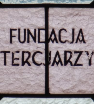 Zdjęcie nr 5: Witraż w kształcie stojącego prostokąta zamkniętego łukiem półkolistym. Kompozycja ujęta geometryczną bordiurą w kolorach czerwonym oraz jasno- i ciemnożółtym. Wewnątrz pole w kształcie stojącego prostokąta zamkniętego łukiem półkolistym z wpisanymi dwoma ostrołukami tworzącymi rodzaj gotyckiego biforium. W jego górnej części motyw kłosów oraz winnych gron. W polu z lewej strony kompozycji owalny medalion mieszczący przedstawienie św. Franciszka z Asyżu ubranego w brązowy habit przepasany sznurem, z kapturem na głowie, umieszczone na tle pejzażu. Święty ukazany frontalnie w tzw. długim popiersiu. W prawej ręce trzyma podwójny krzyż, w lewej otwartą księgę. Wokół głowy nimb. Poniżej medalionu godło tercjarzy (skrzyżowane ręce Chrystusa i św. Franciszka ze śladami po gwoździach w dłoniach, między którymi złoty krzyż na przecięciu ramion z koroną cierniową, u dołu błękitna wstęga) w jasnozielonym polu w kształcie rombu oraz inskrypcja „FUNDACJA / III ZAKON TERCJARZY R(OKU) P(AŃSKIEGO) 1937”. W polu z prawej strony kompozycji owalny medalion mieszczący wizerunek Matki Boskiej Śnieżnej na tle błękitnego nieba. Maria ukazana frontalnie, w tzw. długim popiersiu z głową zwróconą w trzech czwartych w lewo. Lewą ręką podtrzymuje Dzieciątko, prawa dłoń na tej samej wysokości z wyprostowanym palcem wskazującym i środkowym. Maria przedstawiona jako kobieta o owalnej twarzy z dużymi szeroko otwartymi oczami, prostym nosem i niewielkich, wąskich ustach. Jest ubrana w złote szaty – suknię z długimi rękawami oraz bogato zdobiony ornamentem roślinnym płaszcz. Na głowie złota chusta zdobiona ornamentem roślinnym oraz rozbudowana korona w typie zamkniętym zwieńczona krzyżem. Wokół głowy promienisty nimb. Dzieciątko przedstawione w pozycji siedzącej z ciałem zwróconym w trzech czwartych w kierunku Marii. Głowa uniesiona lekko do góry, prawa dłoń wyciągnięta do przodu wykonuje gest błogosławieństwa. W lewej dłoni Dzieciątko trzyma zamkniętą księgę. Postać jest ubrana w złotą tunikę z długimi rękawami zdobioną ornamentem roślinnym. Spod szat widoczne bose stopy. Na głowie Dzieciątka korona w typie zamkniętym zwieńczona krzyżem. Poniżej inskrypcja „FUNDACJA / RÓŻE MĘŻCZYZN I KOBIET R(OKU) P(AŃSKIEGO) 1937” oraz w prawym, dolnym rogu kompozycji sygnatura „Wy[konał] M[aksymilian] Romańczyk / Kraków”. Tło witraża wypełnia ukośna kratownica w kolorach jasnozielonym i białym (szkło bezbarwne).



