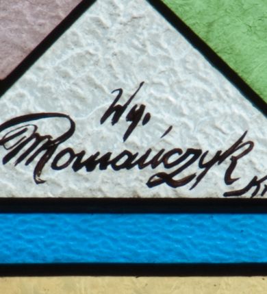 Zdjęcie nr 6: Witraż w kształcie stojącego prostokąta zamkniętego łukiem półkolistym. Kompozycja ujęta geometryczną bordiurą w kolorach czerwonym oraz jasno- i ciemnożółtym. Wewnątrz pole w kształcie stojącego prostokąta zamkniętego łukiem półkolistym z wpisanymi dwoma ostrołukami tworzącymi rodzaj gotyckiego biforium. W jego górnej części motyw kłosów oraz winnych gron. W polu z lewej strony kompozycji owalny medalion mieszczący przedstawienie św. Franciszka z Asyżu ubranego w brązowy habit przepasany sznurem, z kapturem na głowie, umieszczone na tle pejzażu. Święty ukazany frontalnie w tzw. długim popiersiu. W prawej ręce trzyma podwójny krzyż, w lewej otwartą księgę. Wokół głowy nimb. Poniżej medalionu godło tercjarzy (skrzyżowane ręce Chrystusa i św. Franciszka ze śladami po gwoździach w dłoniach, między którymi złoty krzyż na przecięciu ramion z koroną cierniową, u dołu błękitna wstęga) w jasnozielonym polu w kształcie rombu oraz inskrypcja „FUNDACJA / III ZAKON TERCJARZY R(OKU) P(AŃSKIEGO) 1937”. W polu z prawej strony kompozycji owalny medalion mieszczący wizerunek Matki Boskiej Śnieżnej na tle błękitnego nieba. Maria ukazana frontalnie, w tzw. długim popiersiu z głową zwróconą w trzech czwartych w lewo. Lewą ręką podtrzymuje Dzieciątko, prawa dłoń na tej samej wysokości z wyprostowanym palcem wskazującym i środkowym. Maria przedstawiona jako kobieta o owalnej twarzy z dużymi szeroko otwartymi oczami, prostym nosem i niewielkich, wąskich ustach. Jest ubrana w złote szaty – suknię z długimi rękawami oraz bogato zdobiony ornamentem roślinnym płaszcz. Na głowie złota chusta zdobiona ornamentem roślinnym oraz rozbudowana korona w typie zamkniętym zwieńczona krzyżem. Wokół głowy promienisty nimb. Dzieciątko przedstawione w pozycji siedzącej z ciałem zwróconym w trzech czwartych w kierunku Marii. Głowa uniesiona lekko do góry, prawa dłoń wyciągnięta do przodu wykonuje gest błogosławieństwa. W lewej dłoni Dzieciątko trzyma zamkniętą księgę. Postać jest ubrana w złotą tunikę z długimi rękawami zdobioną ornamentem roślinnym. Spod szat widoczne bose stopy. Na głowie Dzieciątka korona w typie zamkniętym zwieńczona krzyżem. Poniżej inskrypcja „FUNDACJA / RÓŻE MĘŻCZYZN I KOBIET R(OKU) P(AŃSKIEGO) 1937” oraz w prawym, dolnym rogu kompozycji sygnatura „Wy[konał] M[aksymilian] Romańczyk / Kraków”. Tło witraża wypełnia ukośna kratownica w kolorach jasnozielonym i białym (szkło bezbarwne).



