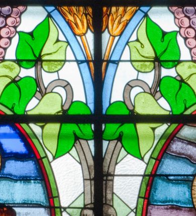 Zdjęcie nr 1: Witraż w kształcie stojącego prostokąta zamkniętego łukiem półkolistym. Kompozycja ujęta geometryczną bordiurą w kolorach czerwonym oraz jasno- i ciemnożółtym. Wewnątrz pole w kształcie stojącego prostokąta zamkniętego łukiem półkolistym z wpisanymi dwoma ostrołukami tworzącymi rodzaj gotyckiego biforium. W jego górnej części motyw kłosów oraz winnych gron. W polu z lewej strony kompozycji owalny medalion mieszczący przedstawienie św. Franciszka z Asyżu ubranego w brązowy habit przepasany sznurem, z kapturem na głowie, umieszczone na tle pejzażu. Święty ukazany frontalnie w tzw. długim popiersiu. W prawej ręce trzyma podwójny krzyż, w lewej otwartą księgę. Wokół głowy nimb. Poniżej medalionu godło tercjarzy (skrzyżowane ręce Chrystusa i św. Franciszka ze śladami po gwoździach w dłoniach, między którymi złoty krzyż na przecięciu ramion z koroną cierniową, u dołu błękitna wstęga) w jasnozielonym polu w kształcie rombu oraz inskrypcja „FUNDACJA / III ZAKON TERCJARZY R(OKU) P(AŃSKIEGO) 1937”. W polu z prawej strony kompozycji owalny medalion mieszczący wizerunek Matki Boskiej Śnieżnej na tle błękitnego nieba. Maria ukazana frontalnie, w tzw. długim popiersiu z głową zwróconą w trzech czwartych w lewo. Lewą ręką podtrzymuje Dzieciątko, prawa dłoń na tej samej wysokości z wyprostowanym palcem wskazującym i środkowym. Maria przedstawiona jako kobieta o owalnej twarzy z dużymi szeroko otwartymi oczami, prostym nosem i niewielkich, wąskich ustach. Jest ubrana w złote szaty – suknię z długimi rękawami oraz bogato zdobiony ornamentem roślinnym płaszcz. Na głowie złota chusta zdobiona ornamentem roślinnym oraz rozbudowana korona w typie zamkniętym zwieńczona krzyżem. Wokół głowy promienisty nimb. Dzieciątko przedstawione w pozycji siedzącej z ciałem zwróconym w trzech czwartych w kierunku Marii. Głowa uniesiona lekko do góry, prawa dłoń wyciągnięta do przodu wykonuje gest błogosławieństwa. W lewej dłoni Dzieciątko trzyma zamkniętą księgę. Postać jest ubrana w złotą tunikę z długimi rękawami zdobioną ornamentem roślinnym. Spod szat widoczne bose stopy. Na głowie Dzieciątka korona w typie zamkniętym zwieńczona krzyżem. Poniżej inskrypcja „FUNDACJA / RÓŻE MĘŻCZYZN I KOBIET R(OKU) P(AŃSKIEGO) 1937” oraz w prawym, dolnym rogu kompozycji sygnatura „Wy[konał] M[aksymilian] Romańczyk / Kraków”. Tło witraża wypełnia ukośna kratownica w kolorach jasnozielonym i białym (szkło bezbarwne).



