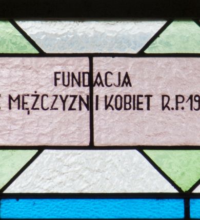 Zdjęcie nr 8: Witraż w kształcie stojącego prostokąta zamkniętego łukiem półkolistym. Kompozycja ujęta geometryczną bordiurą w kolorach czerwonym oraz jasno- i ciemnożółtym. Wewnątrz pole w kształcie stojącego prostokąta zamkniętego łukiem półkolistym z wpisanymi dwoma ostrołukami tworzącymi rodzaj gotyckiego biforium. W jego górnej części motyw kłosów oraz winnych gron. W polu z lewej strony kompozycji owalny medalion mieszczący przedstawienie św. Franciszka z Asyżu ubranego w brązowy habit przepasany sznurem, z kapturem na głowie, umieszczone na tle pejzażu. Święty ukazany frontalnie w tzw. długim popiersiu. W prawej ręce trzyma podwójny krzyż, w lewej otwartą księgę. Wokół głowy nimb. Poniżej medalionu godło tercjarzy (skrzyżowane ręce Chrystusa i św. Franciszka ze śladami po gwoździach w dłoniach, między którymi złoty krzyż na przecięciu ramion z koroną cierniową, u dołu błękitna wstęga) w jasnozielonym polu w kształcie rombu oraz inskrypcja „FUNDACJA / III ZAKON TERCJARZY R(OKU) P(AŃSKIEGO) 1937”. W polu z prawej strony kompozycji owalny medalion mieszczący wizerunek Matki Boskiej Śnieżnej na tle błękitnego nieba. Maria ukazana frontalnie, w tzw. długim popiersiu z głową zwróconą w trzech czwartych w lewo. Lewą ręką podtrzymuje Dzieciątko, prawa dłoń na tej samej wysokości z wyprostowanym palcem wskazującym i środkowym. Maria przedstawiona jako kobieta o owalnej twarzy z dużymi szeroko otwartymi oczami, prostym nosem i niewielkich, wąskich ustach. Jest ubrana w złote szaty – suknię z długimi rękawami oraz bogato zdobiony ornamentem roślinnym płaszcz. Na głowie złota chusta zdobiona ornamentem roślinnym oraz rozbudowana korona w typie zamkniętym zwieńczona krzyżem. Wokół głowy promienisty nimb. Dzieciątko przedstawione w pozycji siedzącej z ciałem zwróconym w trzech czwartych w kierunku Marii. Głowa uniesiona lekko do góry, prawa dłoń wyciągnięta do przodu wykonuje gest błogosławieństwa. W lewej dłoni Dzieciątko trzyma zamkniętą księgę. Postać jest ubrana w złotą tunikę z długimi rękawami zdobioną ornamentem roślinnym. Spod szat widoczne bose stopy. Na głowie Dzieciątka korona w typie zamkniętym zwieńczona krzyżem. Poniżej inskrypcja „FUNDACJA / RÓŻE MĘŻCZYZN I KOBIET R(OKU) P(AŃSKIEGO) 1937” oraz w prawym, dolnym rogu kompozycji sygnatura „Wy[konał] M[aksymilian] Romańczyk / Kraków”. Tło witraża wypełnia ukośna kratownica w kolorach jasnozielonym i białym (szkło bezbarwne).



