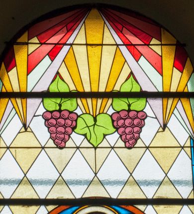 Zdjęcie nr 3: Witraż w kształcie wydłużonego, stojącego prostokąta zamkniętego półkoliście. W centrum kompozycji medalion mieszczący popiersie św. Stanisława Kostki. Święty zwrócony w trzech czwartych w prawo. Twarz owalna, o regularnych rysach. Ręce na wysokości piersi złożone w geście modlitwy. Poniżej bukiet białych lilii. Święty Stanisław ubrany jest w czarną sutannę z białym kołnierzem. Wokół głowy jasnożółty nimb. W górnej części witrażu przedstawione winne grona na tle geometrycznej kompozycji w kolorach żółtym i czerwonym. W dolnej strefie witrażu inskrypcja „FUNDACJA / MŁODZIEŻY MĘSKIEJ R(OKU) P(AŃSKIEGO) 1937”. Tło kompozycji wypełnione motywem rombów w kolorach jasnożółtym i białym.

