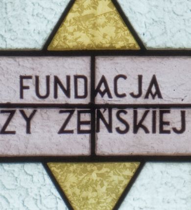 Zdjęcie nr 3: Witraż w kształcie wydłużonego, stojącego prostokąta zamkniętego półkoliście. W centrum kompozycji umieszczony medalion mieszczący popiersie św. Teresy z Lisieux trzymającej krucyfiks i róże. Święta ukazana frontalnie z głową zwróconą w trzech czwartych w lewo. Twarz owalna, o regularnych rysach, z dużymi oczami, wąskim nosem oraz niewielkimi ustami. Święta w rękach złożonych na wysokości piersi trzyma bukiet czerwonych i różowych róż oraz krucyfiks, na który spływają promienie. Teresa ubrana jest w brązowy karmelitański habit z białym płaszczem oraz białą toką i czarnym welonem na głowie. Tło medalionu utrzymane jest odcieniach niebieskiego. Wokół głowy jasnożółty nimb. W górnej części witrażu przedstawione winne grona na tle geometrycznej kompozycji w kolorach żółtym i czerwonym. W dolnej strefie witrażu inskrypcja „FUNDACJA / MŁODZIEŻY ŻEŃSKIEJ R(OKU) P(AŃSKIEGO) 1937” oraz poniżej, w lewym, dolnym rogu sygnatura: „Wy[konał] / M[aksymilian]Romańczyk / Kraków św. Jana 30”. Tło kompozycji wypełnione motywem rombów w kolorach jasnożółtym i białym.