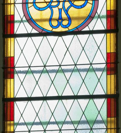 Zdjęcie nr 2: Witraż w kształcie stojącego prostokąta zamkniętego półkoliście ujęty geometryczną bordiurą dekorowaną czerwonymi i żółtymi prostokątami. W polu ukośna kratka wypełniona białymi i jasnozielonymi rombami. W górnej części witraża okrągły medalion z niebieskim monogamem maryjnym umieszczonym na żółtym tle. W dolej kwaterze prostokątne pole z napisem: „FUNDACJA / MAGDALENA HARDENOWA R[OKU] P[AŃSKIEGO] 1937.” 